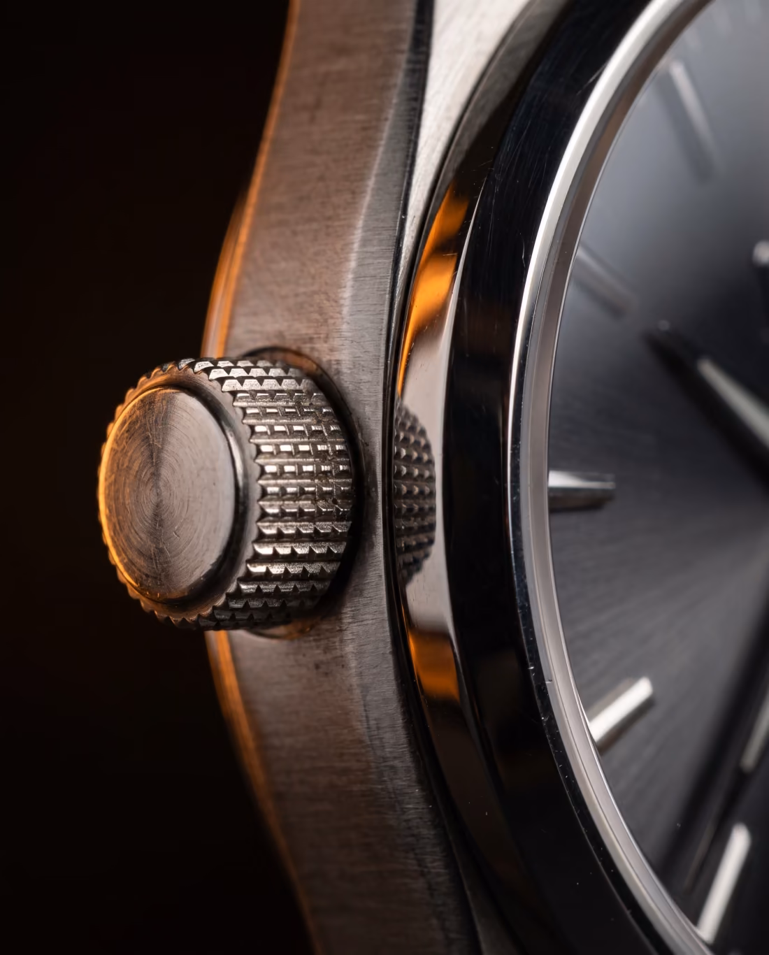 Extreme close-up of a knurled watch crown and the brushed and polished flank of the steel case.