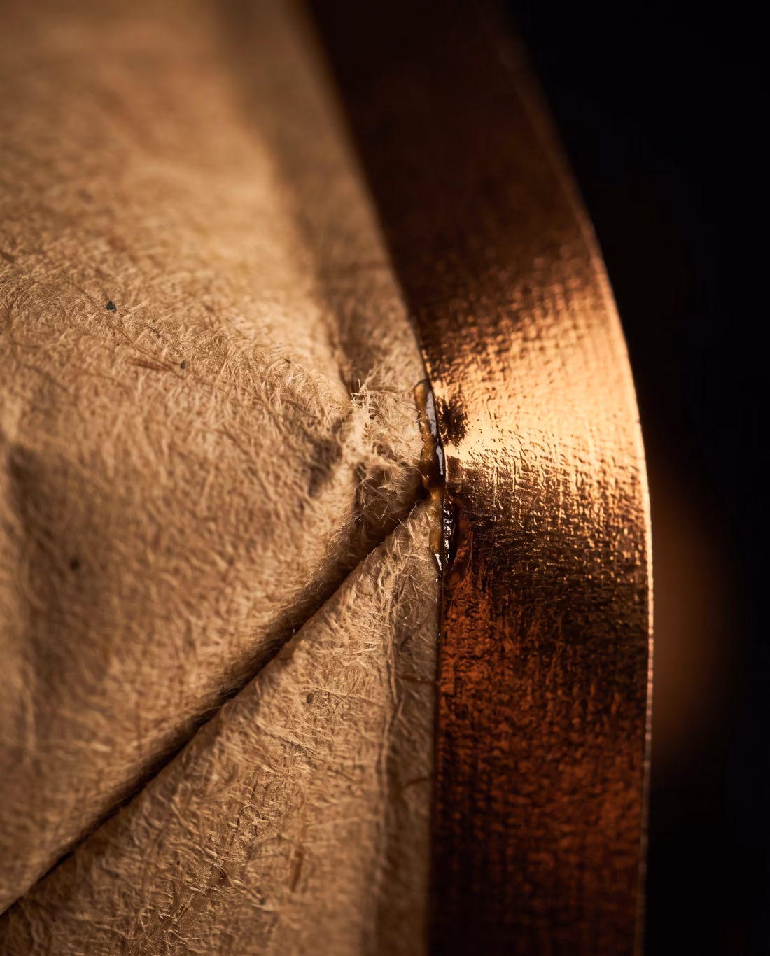 Extreme close-up of a kraft paper packaging seam meeting a bronze foil edge.
