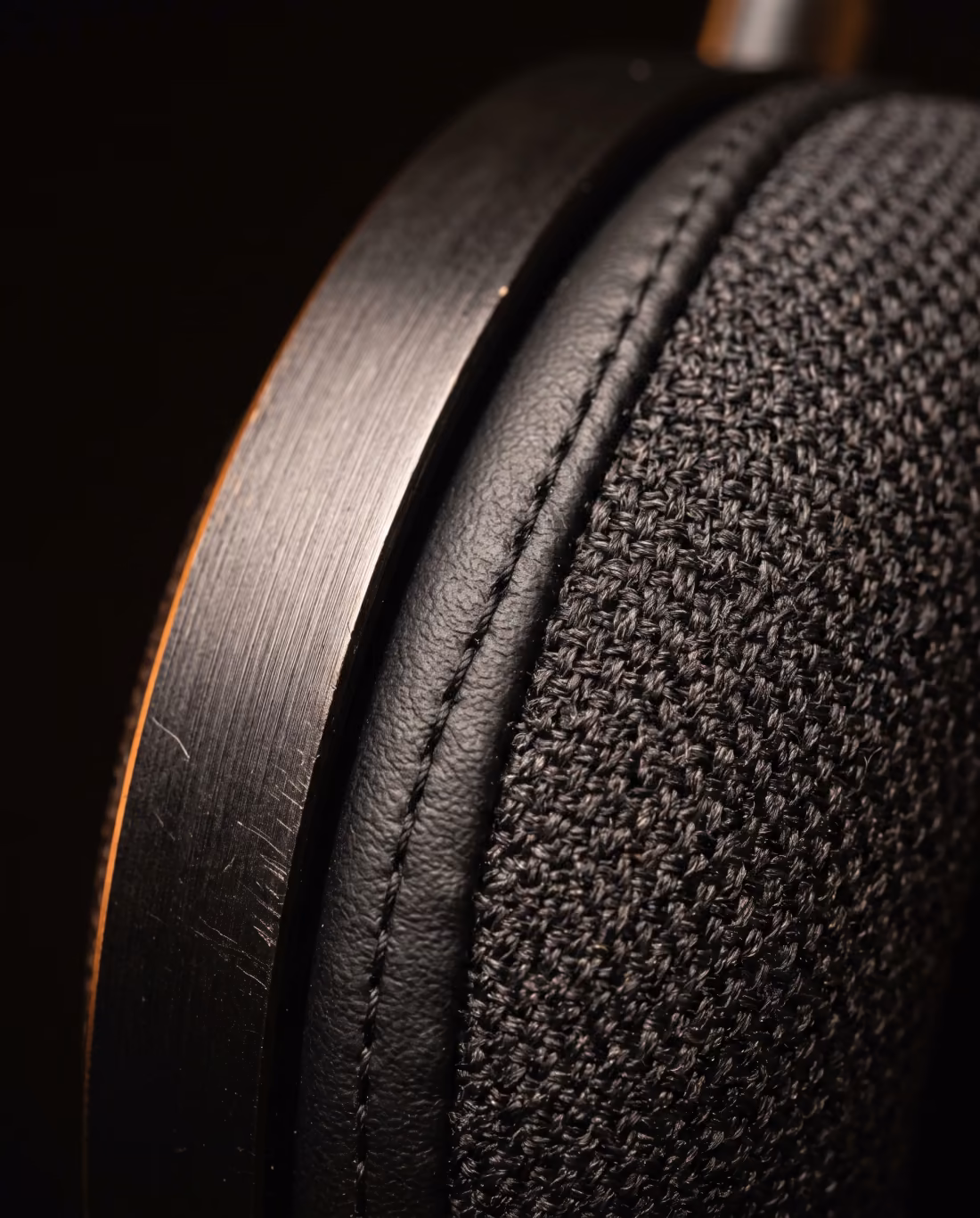 Extreme close-up of the headphone earcup showing woven acoustic mesh, stitched cushion and a brushed aluminum edge.