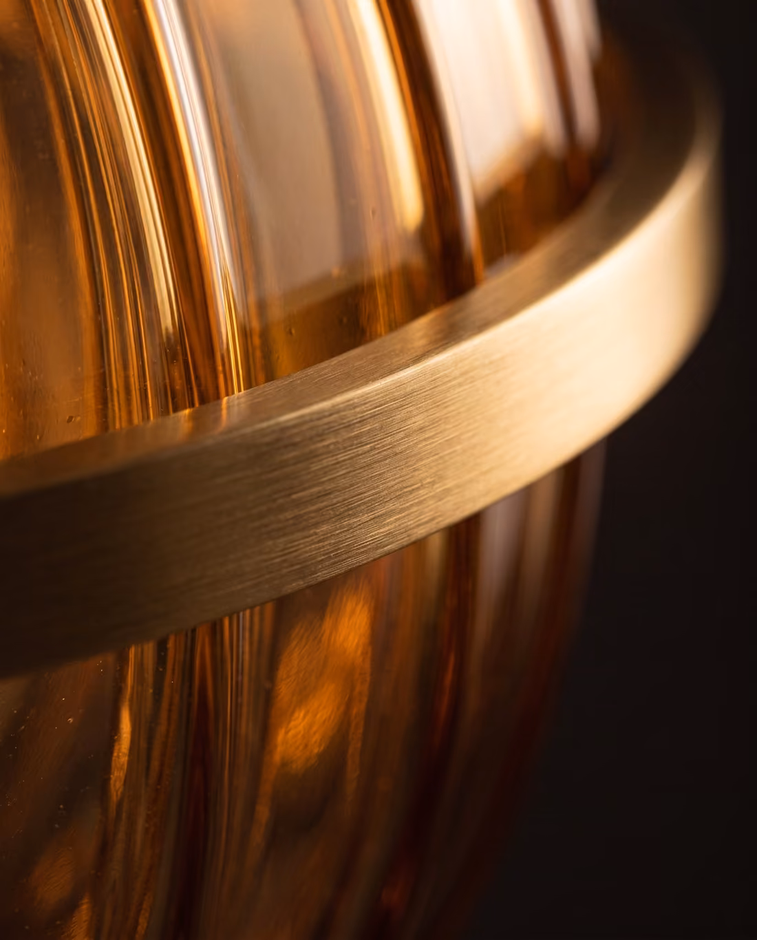 Close-up of the brushed brass ring wrapping the ribbed amber glass globe.