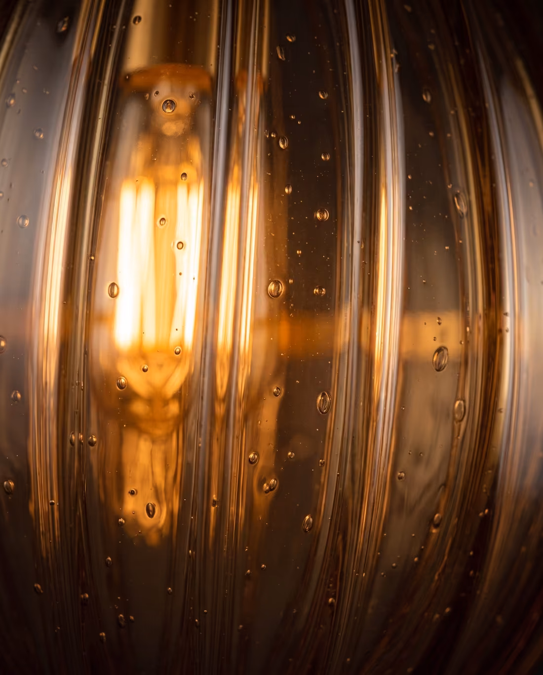 Close-up of the ribbed amber glass, with trapped air bubbles and the glowing filament inside.