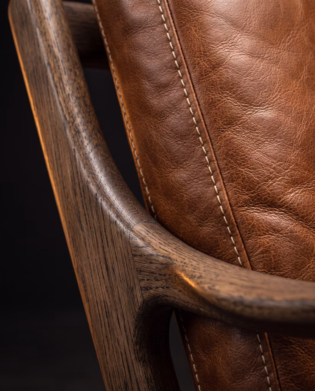 Close-up where the curved oak armrest meets the stitched cognac leather back cushion.