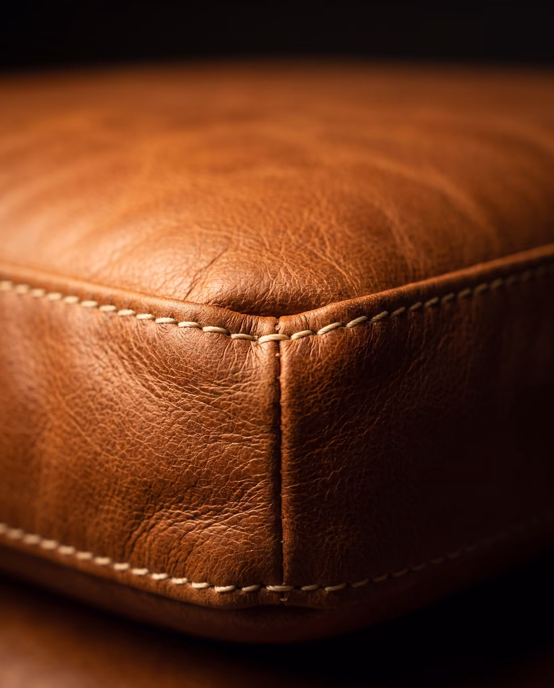 Close-up of the cognac leather cushion edge, showing the natural grain and cream contrast top-stitching.