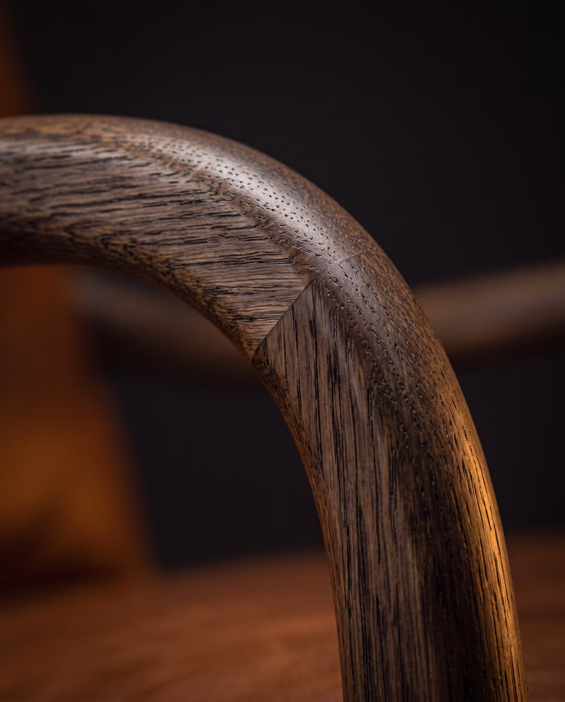 Close-up of the smoked oak armrest curving into the front leg, showing the open grain.