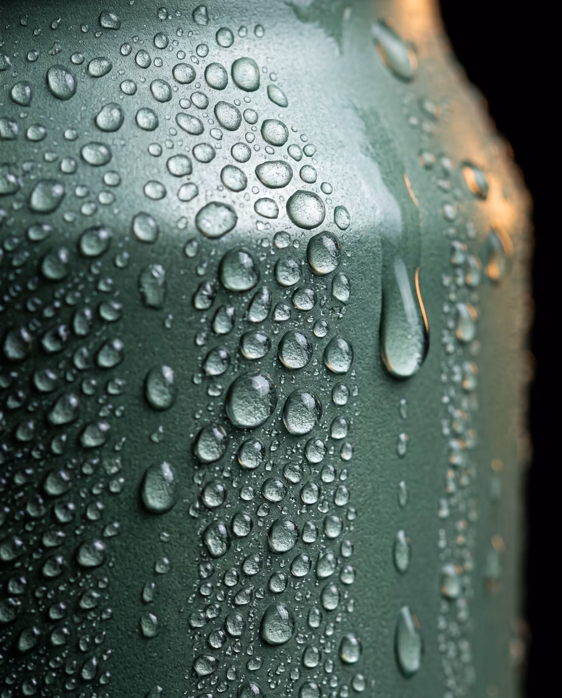 Extreme close-up of condensation droplets beaded on a matte sage-green aluminum can surface.