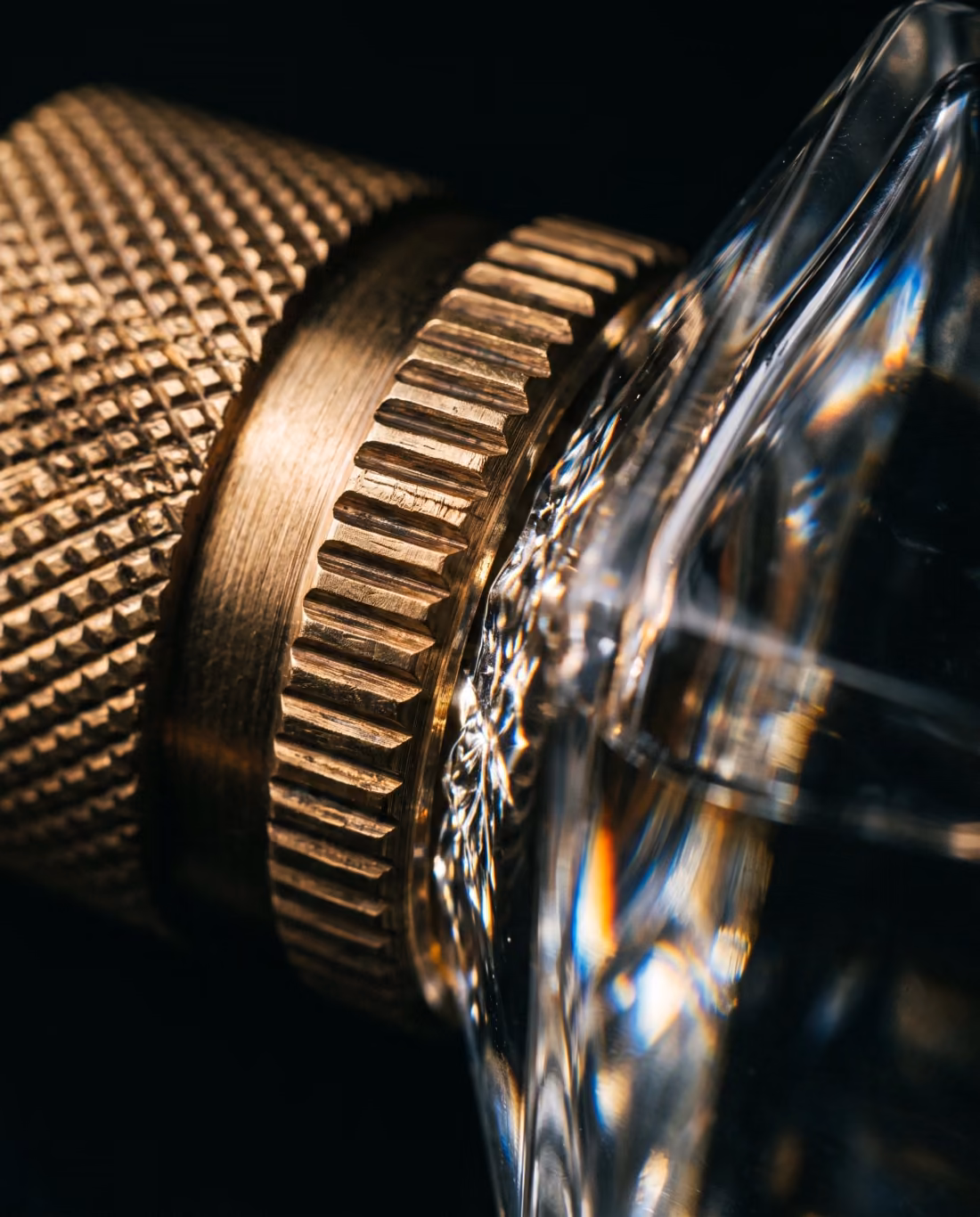 Extreme close-up of a knurled brass perfume cap meeting a thick beveled glass edge.